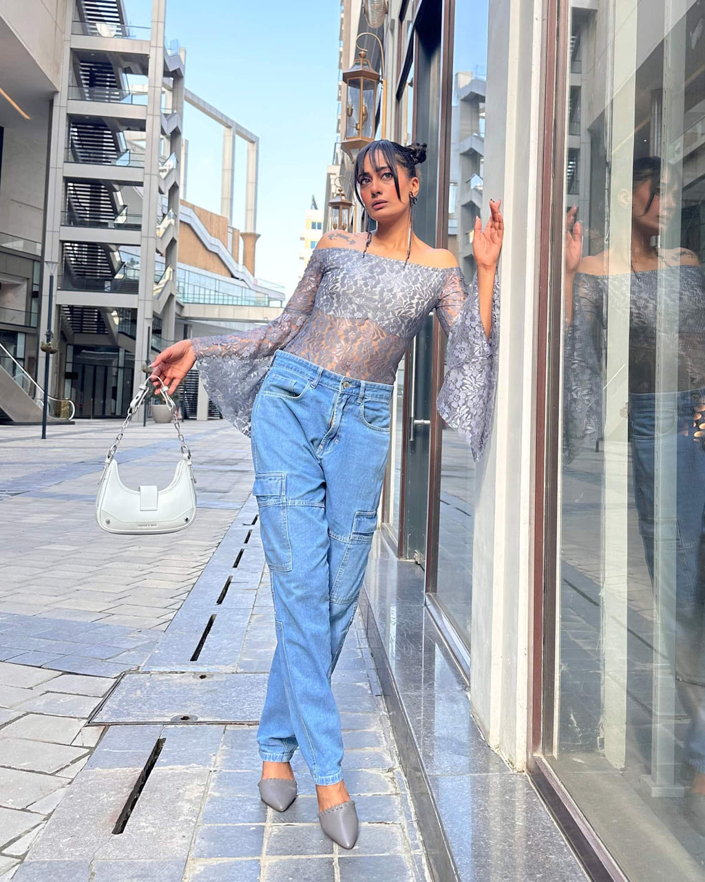 Model wearing a grey lace bodysuit for women with off-shoulder styling, long flounce sleeves, semi-sheer fabric, and front lining for comfort.